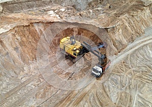 Largest mining excavator with electric shovel loading sand into dump truck in opencast. Orange mining trucks transports sand in