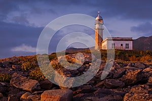 Larino Lighthouse surrounded by rocks during the sunset in Spain photo