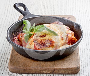 Lasagna in a cast iron pan on a wooden board. Traditional Italian dish