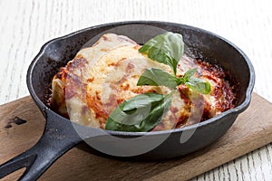 Lasagna in a cast iron pan on a wooden board. Traditional Italian dish