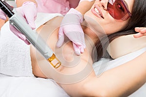 Laser cosmetology Armpit hair removal. Beautiful smiling woman client in red glasses having procedure.