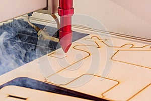 Laser engraver working and engraving wooden board with smoke