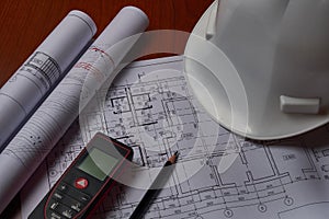 Laser meter, white hardhat and drawings at engineer workplace