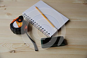 Laser range finder, tape measure, notebook, pencil on a light background