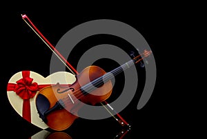 Classic violin with bow and a heart shape gift box on dark background