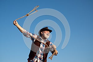 Lasso throwing. Old wild west cowboy with rope. Bearded western man with brown jacket and hat catching horse or cow.