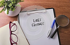 Last Chance word on paper with glass ballpen and green plant.