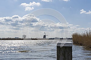 The last mooring post of a boat dock in the lake de Rottemeren with the windmill Tweemanspolder nr 4 in the background on a sunny