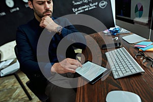 Last news. Young businessman man sitting at his workplace in the modern office and reading financial business news
