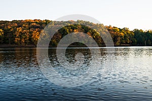 Last rays of sun on bank of lake with forest. Beautiful scenic panoramic autumn view. Golden hour.