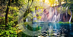Last sunlight lights up the pure water waterfall on Plitvice National Park. Colorful spring panorama of green forest with blue