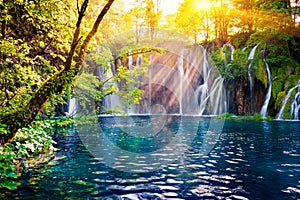 Last sunlight lights up the pure water waterfall on Plitvice National Park. Colorful spring scene of green forest with blue lake.