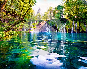 Last sunlight lights up the pure water waterfall on Plitvice National Park. Spectacular spring scene of green forest with blue