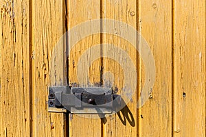 Latch on yellow wooden wall. Old shabby wooden planks with cracked color paint