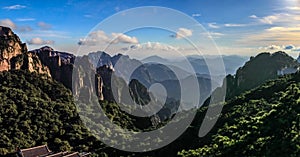 Late afternoon casts long shadows on the lush green pine trees with many mountain ranges fading towards the horizon in Huang Shan