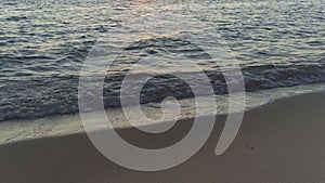 Late afternoon sun just before sunset, shines on wet sandy beach and calm sea, closeup to small water waves