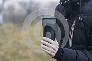 In late autumn, men`s hands are warming themselves on a black toggle switch with a hot drink. Environmentally friendly use of photo
