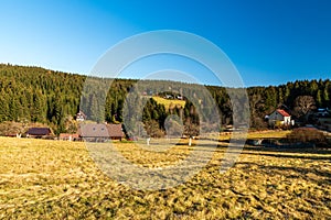 Late autumn scenery with meadow, few buildings, hill covered by forest and clear sky