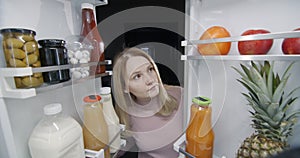 Late at night, a woman looks inside a large refrigerator. Night snack concept