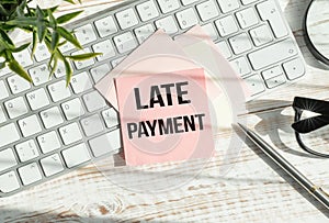 Late Payment text on sticky with keyboard, pen glasses on grey background photo