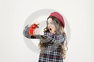 She is late for school. Small child punching alarm clock with anger on yellow background. Angry little girl fighting