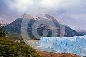 Lateral view of Perito Moreno Glacier, in El Calafate, Argentina, against a grey and cloudy sky and dramatic mountains