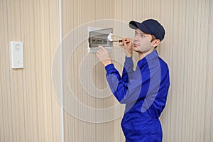 Lateral view of a young electrician in blue overall disassembling a electrical panel