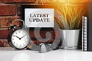LATEST UPDATE text with alarm clock, books and vase on brick background