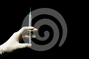 Latex gloved hand holding syringe against a black background