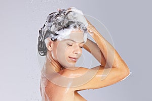 Lather, rinse and repeat. Studio shot of an attractive young woman washing her hair while taking a shower against a grey