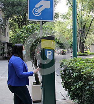 Latin adult woman with protection mask paying public parking on the street, new normal covid-19