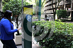 Latin adult woman with protection mask paying public parking on the street, new normal covid-19