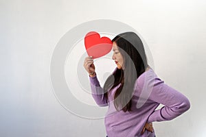 Latin adult woman with red heart shows her sadness, anger and unhappiness for the arrival of February and celebrating Valentine`s