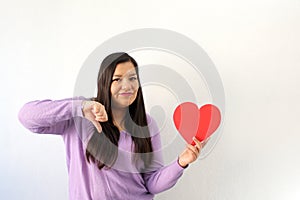 Latin adult woman with red heart shows her sadness, anger and unhappiness for the arrival of February and celebrating Valentine`s