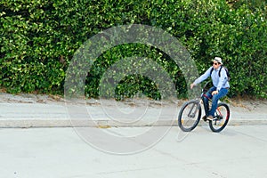 A Latin American businessman in business casual clothes and sunglasses on a bicycle on his way to his workplace on a city street