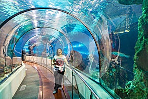 Latin American chubby smiling female tourist standing under glass tunnel of big pond