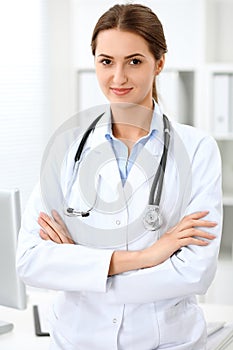 Latin american doctor woman standing with arms crossed and smiling at hospital. Physician ready to examine patient