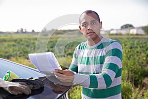 Latin american farmworker signing papers near car on field photo