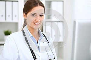 Latin american female doctor sitting at the table and working by computer at hospital office. The physician or therapist