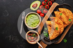 Latin American, Mexican, Chilean food. Traditional fried empanadas served with tomato and avocado sauce on a dark background. Top