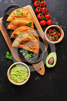 Latin American, Mexican, Chilean food. Traditional fried empanadas served with tomato and avocado sauce on a dark background. Top