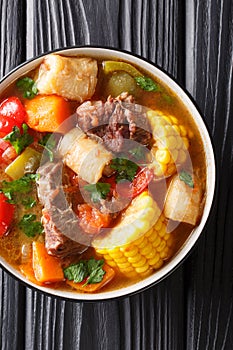 Latin American Sancocho thick meat soup with vegetables close-up on a plate on the table. Vertical top view photo