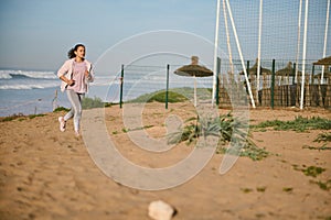 Latin American sportswoman, athlete, runner enjoying her cardio workout outdoor, running on the sandy beach at sunset.