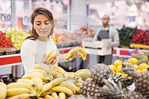 Latin american woman choosing sweet bananas in supermarket