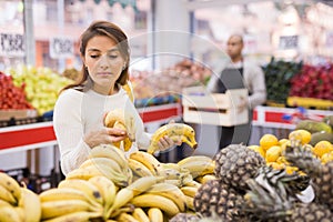 Latin american woman choosing sweet bananas in supermarket