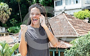 Latin american young adult man with dreadlocks cheering on phone