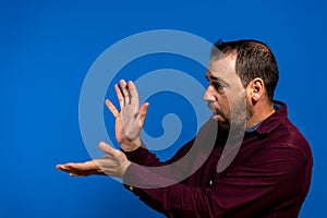 Latin bearded man dressed in a purple shirt isolated on blue studio background, he is throwing a kame hame imitating Son