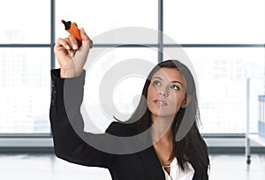 Latin business woman in formal suit writing with marker on invisible virtual screen or board at modern office