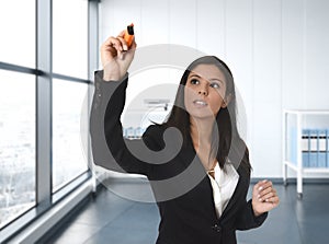 Latin business woman in formal suit writing with marker on invisible virtual screen or board at modern office