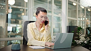 Latin busy office worker multitasking, making a client call at her desk.